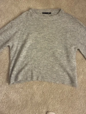 Ljusgrå stickad tröja Lager 157 - Mysig ljusgrå stickad tröja med rund halsringning och långa ärmar. Tröjan har en enkel, rak passform och ribbade muddar vid ärmslut och nederkant. Perfekt för lager på lager och chill vardagsstil.