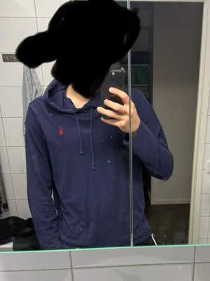 Mörkblå hoodie från Polo Ralph Lauren - Säljer en mörkblå hoodie från Polo Ralph Lauren med klassisk röd logga på bröstet. Hoodien har huva med dragsko och är tillverkad i ett mjukt material som är skönt att bära. Perfekt för dig som gillar stilrena och tidlösa plagg.