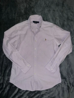  skjorta från polo Ralph Lauren - Klassisk ljuslila skjorta från Ralph Lauren med button-down krage och broderad polospelare på bröstet. Skjortan har långa ärmar, vita knappar och är tillverkad i bomull. Perfekt för en stilren och avslappnad look. Bara att skriva för fler bilder om ni vill ha nummret för suppliern osv.  Pris kan diskuteras vid snabb affär!