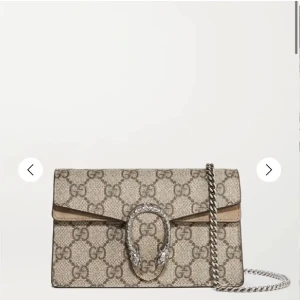 Gucci Dionysus GG Supreme kuvertväska - Säljer en beige och brun dupe Gucci Dionysus kuvertväska i GG Supreme canvas med ikoniskt monogrammönster. Väskan har ett dekorativt spänne framtill och en silverfärgad kedjerem. Perfekt för dig som vill ha en lyxig och trendig accessoar. Pris kan diskuteras vid snabb köp 