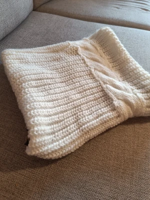 Vit stickad halsduk med flätmönster - Mysig vit stickad halsduk i tjockt garn med ett snyggt flätmönster på ena sidan. Perfekt för kalla dagar och ger en stilren look till din outfit. Materialet känns mjukt och värmande, och halsduken har en klassisk, tidlös design. Tub Djurmönstrat mjuk tyg på insidan. 