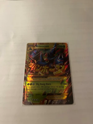 Pokémonkort Mega Heracross EX - Säljer ett samlarkort från Pokémon, Mega Heracross EX med holografisk yta och japansk text. Kortet har färgstarka detaljer i blått, gult och rött och är en del av Pokémon TCG-serien. Perfekt för dig som gillar att samla eller spela Pokémonkort.
