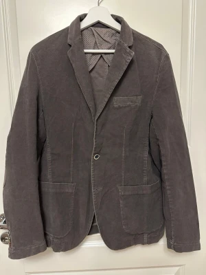 Brun kavaj från FB - Brun FB kavaj, strl 50. Elastan, Polyester. Ärmlängd (cm) 67 , Axelbredd (cm) 49. Urtvättad/Slitet .