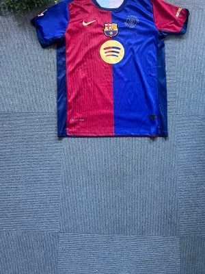 Barcelona matchtröja Nike blå/röd - Säljer en officiell FC Barcelona matchtröja från Nike i klassiska blå och röda färger. Tröjan har klubbmärke, Nike-logga och sponsortryck på bröstet. Tillverkad i lätt och ventilerande material, perfekt för fotboll eller träning.