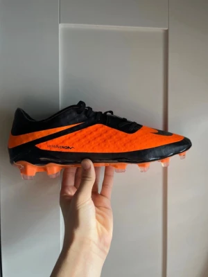 Nike Hypervenom fotbollsskor orange/svart - Säljer ett par Nike Hypervenom fotbollsskor i orange och svart med cool dödskalle-detalj på hälen. Skorna har syntetiskt material med NIKESKIN för extra bra bollkontroll och grepp. Lätta dobbar för spel på gräsplan. Perfekta för dig som vill sticka ut på planen.