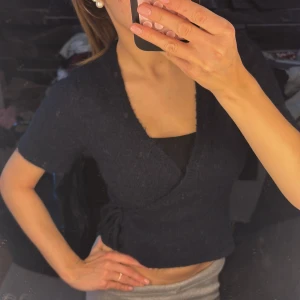 Mörkblå croppad topp med snörning - Snygg mörkblå croppad topp med korta ärmar och v-ringning. Toppen har snörning i sidan som ger en cool detalj och sitter tajt mot kroppen. Perfekt till jeans eller kjol för en trendig look.