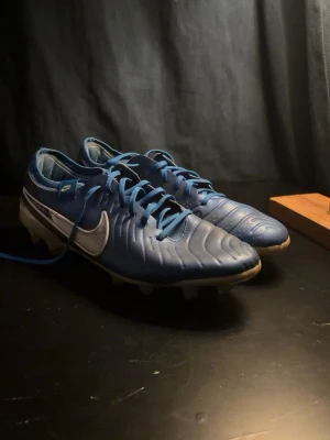 NIKE TIEMPO LEGEND 10 ELITE  MAD AMBITION - SVART/VIT - Säljer ett par blå Nike fotbollsskor med vita detaljer och klassisk swoosh på sidan. Skorna har snörning och slitstarka dobbar för bra grepp på planen. Tillverkade i syntetmaterial med en stilren, sportig design som passar perfekt för matcher och träning.