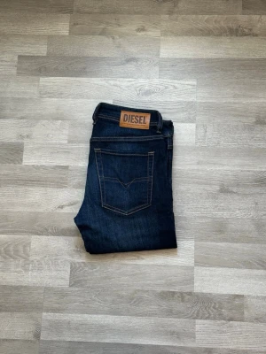 Mörkblå jeans från Diesel - Snygga mörkblå jeans från Diesel med klassisk femficksdesign och kontrastsömmar. Jeansen har en rak passform och ett brunt läderpatch med Diesel-loggan bak i midjan. Tillverkade i slitstarkt denimtyg som ger en tidlös look.