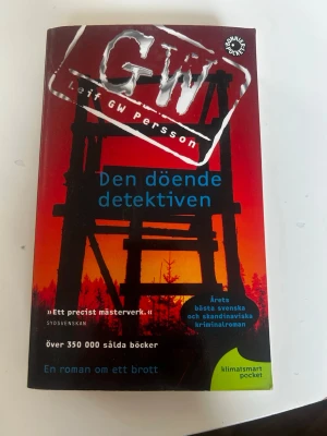 Den döende detektiven pocket - Spännande kriminalroman av Leif GW Persson i pocketformat. Omslaget är rött och svart med siluett av ett torn mot en solnedgång. Boken handlar om Lars Martin Johansson och ett ouppklarat mordfall. Perfekt för dig som gillar deckare och svensk spänning.