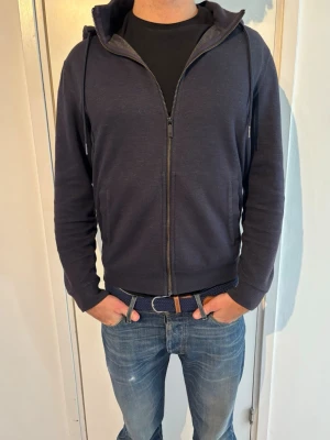 Massimo Dutti zip hoodie - Snygg mörkblå hoodie med dragkedja från Massimo Dutti. Klassisk modell med huva och dragsnören, två fickor framtill och ribbade muddar vid ärmar och nederkant. Tillverkad i mjukt bomullsmaterial som känns skönt mot huden. Perfekt till jeans eller joggers.