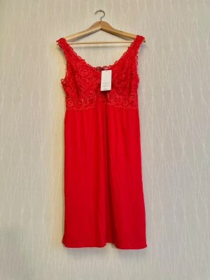 Rött spetsnattlinne  - Snyggt nattlinne i färgen tango red med spetsdetaljer upptill och breda axelband. Modellen är ärmlös och har en mjuk, följsam passform. Perfekt för dig som vill ha något bekvämt och stilrent till natten.