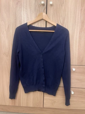 Mörkblå klassisk kofta - En stilren mörkblå kofta med v-ringning och knäppning framtill. Långärmad modell i mjukt, tunt material som passar perfekt till lager på lager. Enkel och tidlös design som funkar till det mesta.