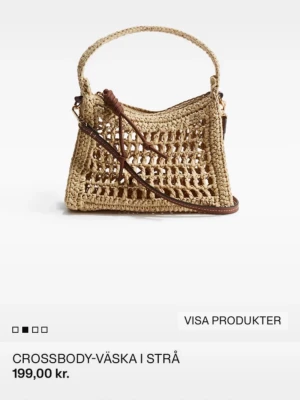 Beige axelväska i strå med flätad design - Säljer en beige axelväska i strå med öppen, flätad design och bruna detaljer. Väskan har både ett kort handtag och en lång axelrem i läderimitation med knutdetaljer. 