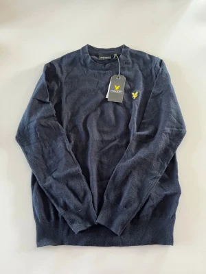 Helt ny Mörkblå stickad tröja Lyle & Scott - Mörkblå stickad tröja från Lyle & Scott med rund halsringning och den klassiska gula logon broderad på bröstet. Tröjan har långa ärmar och ribbade muddar vid ärmslut och nederkant. Perfekt för dig som gillar stilren och enkel design. Ny pris 899kr nu endast 600kr helt ny 