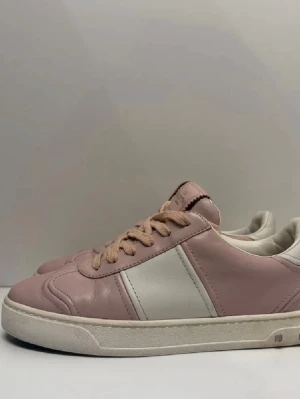 Valentino flycrew - Snygga sneakers i rosa och vitt läder från Valentino. Skorna har klassisk låg profil, vita sidor och rosa detaljer samt matchande rosa skosnören. Yttersulan är vit med små nitar baktill för en extra touch. Perfekta för dig som gillar stilrena men ändå unika sneakers.