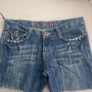 Lågmidjade 2000s tal jeansshorts  - Säljer ett par blå jeansshorts med pärldetaljer och broderade fickor både fram och bak. Shortsen har låg midja, slitningar och rå kant nedtill!