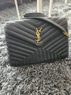 Svart YSL handväska i läder - Säljer en svart handväska från YSL.   Jag har använt väskan vid 2 tillfällen så den är i jättefint skick och har  justerbar axelrem i läder och metall. Perfekt för dig som vill ha en lyxig accessoar med klassisk design. Modellen heter Envelope & är Medium Size. Skickas i dustbag & medföljer kartong vid köp. 