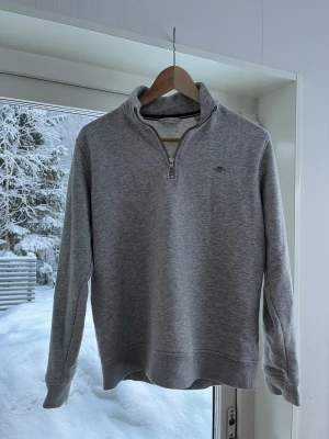 Grå halvzip sweatshirt från Gant - Snygg grå sweatshirt från Gant med halv dragkedja och liten broderad logga på bröstet. Tröjan har en klassisk passform, ribbade muddar och är tillverkad i mjukt bomullsmaterial. Perfekt för en avslappnad och stilren look.