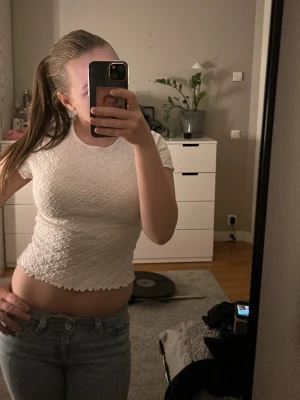 Vit topp med strukturmönster - Säljer en vit topp med korta ärmar och snyggt strukturmönster. Toppen har vågig kant nertill och vid ärmslut, vilket ger en trendig look. Perfekt att matcha med jeans eller kjol för en cool stil. OBS! Linnet är köpt från Kappahl’s barnavdelning och är i storlek 170. Storlek 34-36.