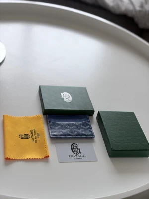 Goyards wallet blå - Snygg blå korthållare med klassiskt mönster i vitt och grått. Tillverkad i canvas och läder, perfekt för kort och ID. Kommer med original ask, tygpåse och äkthetskort. En stilren accessoar för dig som gillar exklusiva detaljer.