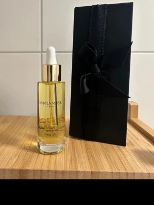 Sunnamusk Fine Oil parfymolja - Exklusiv parfymolja från Sunnamusk London i en elegant glasflaska med gulddetaljer och pipett. Oljan har en gyllene färg och kommer i en lyxig svart presentförpackning med sidenband. Perfekt för dig som vill ha en unik och långvarig doft.