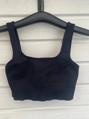 Svart ribbad bh från Aim'n - Svart ribbad bh från Aim'n med breda axelband och fyrkantig ringning. Bh:n är tillverkad i ett stretchigt och bekvämt material som formar sig efter kroppen. Liten metallogo framtill för en stilren touch. Perfekt för dig som gillar en sportig och enkel look.
