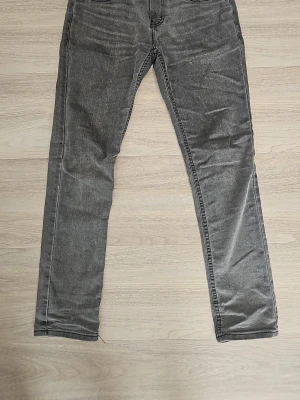 Grå slim taper 512 från Levi's - Snygga grå slim fit jeans från Levi's med klassisk femficksdesign och dragkedjegylf. Jeansen har en tvättad look och raka ben, perfekta för en avslappnad stil. Materialet är mjukt denim som sitter skönt hela dagen. Modell 512 slim taper i grå. Storlek 16a. Pris kan diskuteras, hör gärna av er!
