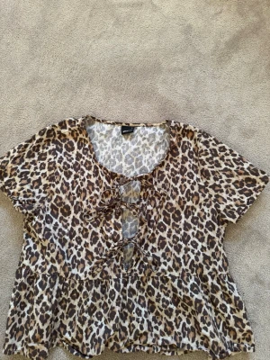 Leopardmönstrad blus från Gina Tricot - Snygg blus från Gina Tricot i leopardmönster med korta ärmar och snörning framtill. Modellen är luftig och har en lätt volang nertill. .