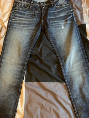 Jack & Jones  - Säljer ett par blå skinny jeans från Jack & jones med snygga slitningar och ljusa partier framtill. Jeansen har klassisk femficksmodell, dragkedjegylf och är tillverkade i stretchigt denim för en bekväm passform fast alla taggs e av.