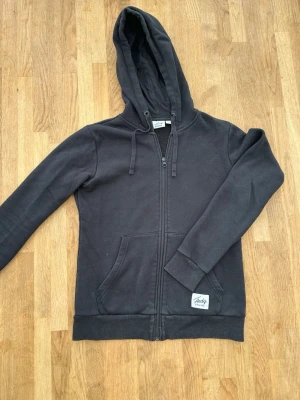 Svart zip hoodie från Andy - Klassisk svart hoodie med dragkedja från Andy. Hoodien har huva med dragsko, två fickor framtill och ribbade muddar vid ärmar och nederkant. Tillverkad i mjukt sweatshirtmaterial, perfekt för en avslappnad stil.
