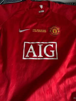 Man utd Ronaldo moscow finalen 2008 - Röd Manchester United matchtröja från Nike med AIG som sponsor, klubbmärke och texten 'FINAL MOSCOW 2008' på bröstet. På ryggen står det 'Ronaldo' och nummer 7 i vitt. Perfekt för fotbollsfans och samlare.