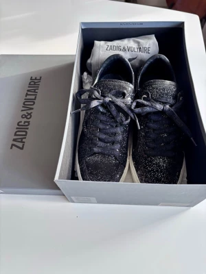 Glittriga svarta sneakers Zadig & Voltaire - Snygga svarta sneakers från Zadig & Voltaire med glittrig finish och vita sulor. Skorna har klassisk låg modell med svarta skosnören och diskret logga på plösen. Perfekta skor inför vår/sommar💕självklart äkta! Säljer då de inte kommer till användning 
