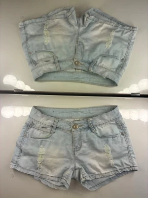 Ljusblå jeansshorts med  låg midja och slitningar samt neondetaljer från Ad’oro jeans - Snygga ljusblå jeansshorts med slitna neon detaljer framtill som lyser igenom slitningarna, vilket ger en mycket cool effekt. Shortsen har klassisk femficksdesigne och har  knapp- och dragkedjestängning. Perfekta för varma dagar och enkel att matcha med olika toppar. Passar både till stranden och festival!☀️
