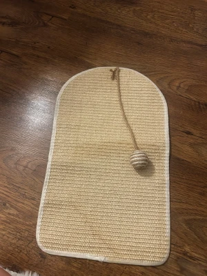 Beige klösbräda med boll - Säljer en beige klösbräda för katt i vävt sisal-liknande material. Brädan har rundade hörn och en fastsatt boll i snöre för extra lek. Perfekt för att hålla kattens klor i trim och ge lite underhållning. Aldrig använts av mina katter