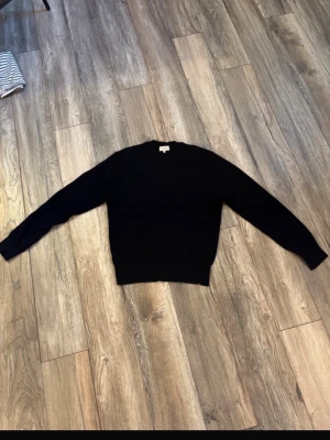 Svart stickad tröja från Sandö - Klassisk svart stickad tröja från Sandö med rund halsringning och ribbade muddar vid ärmslut och nederkant. Enkel och stilren design som passar till det mesta. Perfekt basplagg för garderoben. Enda defekten är på bild 3, ganska kort så är mer en XS