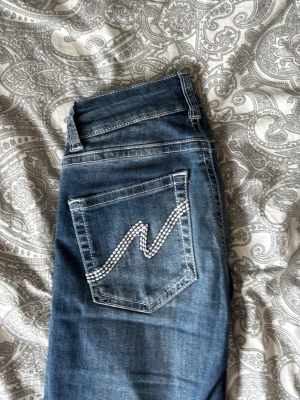 Blå jeans med detaljer från Nelly - Säljer ett par blå jeans från Nelly med snygga kontrastsömmar och dubbla knappar i midjan. Bakfickan har en cool vit zigzag-detalj som sticker ut. Klassisk femficksmodell i denim med normal passform. Säljer då de inte har kommit till andvändning på ett tag. Fint skick men de är använda. 💛