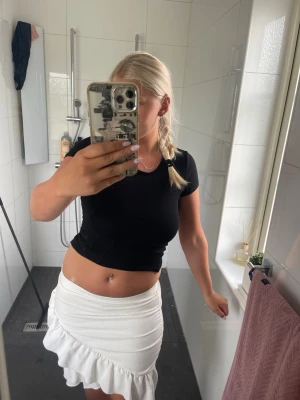 Vit volangkjol med ribbad struktur - Säljer en vit kortkjol med volangkant och ribbad struktur. Kjolen har en figurnära passform och är tillverkad i ett stretchigt material som ger en snygg siluett. Perfekt för sommarens alla tillfällen!