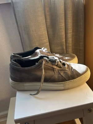 Axel arigato skor  - Snygga sneakers i grå mocka med klassisk låg profil och vita, tjocka gummisulor. Skorna har matchande grå skosnören och diskreta sömdetaljer på sidan. Perfekta för en clean och stilren look.