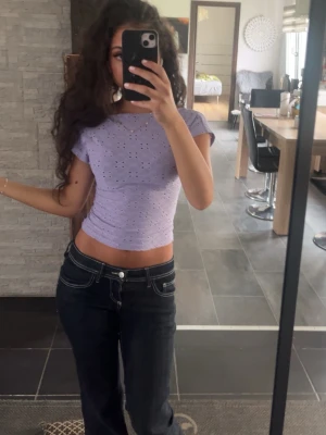 Ljuslila croppad topp med hålmönster - Säljer en ljuslila croppad topp med korta ärmar och hålmönster. Toppen har en slim passform och är perfekt för dig som gillar en söt och trendig stil. 