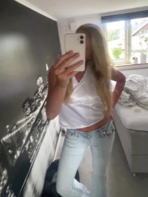 Vit omlottopp i satin med knyte - Säljer en snygg vit omlottopp i satin med knyt i nacken. Toppen är ärmlös och har en lätt glansig finish som ger en lyxig känsla. Perfekt att styla med jeans eller kjol för en trendig look. Toppen är i halterneckmodell. 