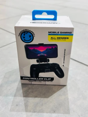 TriggerHappy Controller Clip - Säljer en TriggerHappy Controller Clip för mobil gaming. Fästet är svart och designat för att hålla din smartphone på en handkontroll. Passar till alla genrer och har 180 graders rotation för flexibel spelupplevelse. Perfekt för dig som vill spela mobilspel med handkontroll.