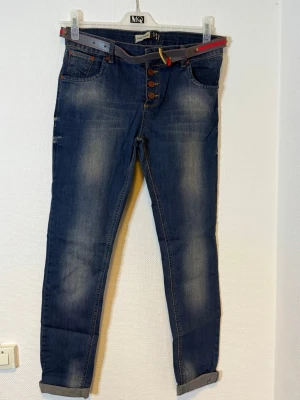 Blå jeans med färgglatt bälte - Midjan 41 cm  Längd 95 cm  Benvidd 24 cm 