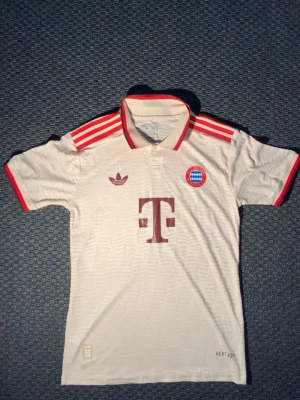 Beige Bayern München tröja Adidas - Säljer en beige Bayern München matchtröja, som använts nåra få gånger och som inte har nåra täcken på användning, alltså är den i ny skick! Tröjan är från Adidas med röda detaljer och klassiska ränder på axlarna. Tröjan har klubbmärke, Adidas-logga och T-Mobile sponsortryck på bröstet. Tillverkad i lätt och ventilerande material. Passar perfekt för allting! 