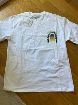 Vit Casablanca t-shirt med tryck - Snygg vit t-shirt från Casablanca med färgglatt tryck av ett fönster och gröna blad på bröstet och ryggen. Klassisk passform och rund halsringning. Perfekt för dig som vill ha en unik och trendig tee med cool grafik.