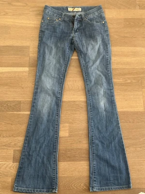 Lågmidjade bootcut jeans - Säljer ett par blå bootcut jeans med snygga detaljer på bakfickorna. Köpta secondhand, men i fint skick. Midjemått: 35 cm Innerbenslängd: 80 cm 💕💕