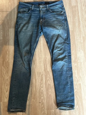 Blå slim fit jeans från Jack & Jones - Säljer ett par blå slim fit jeans från Jack & Jones med klassisk femficksmodell och snygga slitningar framtill och baktill. Jeansen har normal midja, dragkedjegylf och är tillverkade i bomull med lite stretch för skön passform.