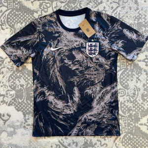 England Nike VM fotbollströja - S/M - England fotbollströja från Nike med ett mönster i svart, grått och beige. Storleken är S men den är genuint M. Så om du tar på dig M så kommer den passa dig. Pris kan diskuteras