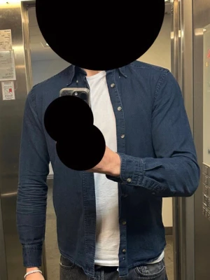 Mörkblå skjorta  - Snygg mörkblå jeansjacka med klassisk passform och knappar framtill. Jackan har långa ärmar och är tillverkad i ett mjukt denimtyg. Perfekt för dig som gillar en stilren och tidlös look.