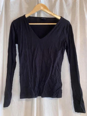 Svart långärmad v-ringad topp - En enkel och stilren svart långärmad topp med v-ringning. Toppen har en smal passform och är tillverkad i mjuk bomull, perfekt att matcha med jeans eller kjol för en clean look.
