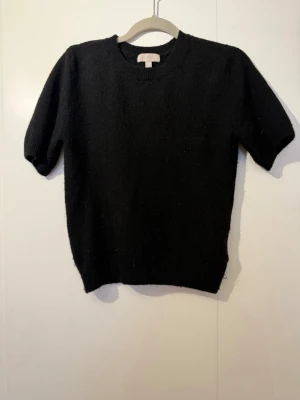 Svart stickad tröja med kort ärm - En enkel och stilren svart stickad tröja med korta ärmar och rund hals. Tröjan har ribbade muddar vid ärmslut och nederkant. Perfekt att matcha med jeans eller kjol för en clean look🥰 